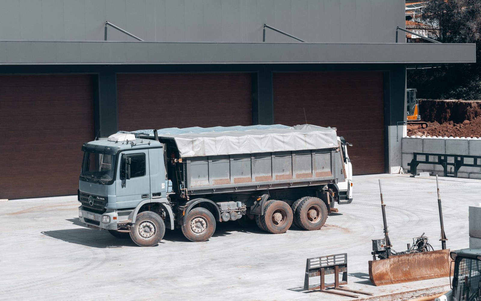 A tarpaulin-covered dump truck parked outside roll-up doors at a warehouse loading area
