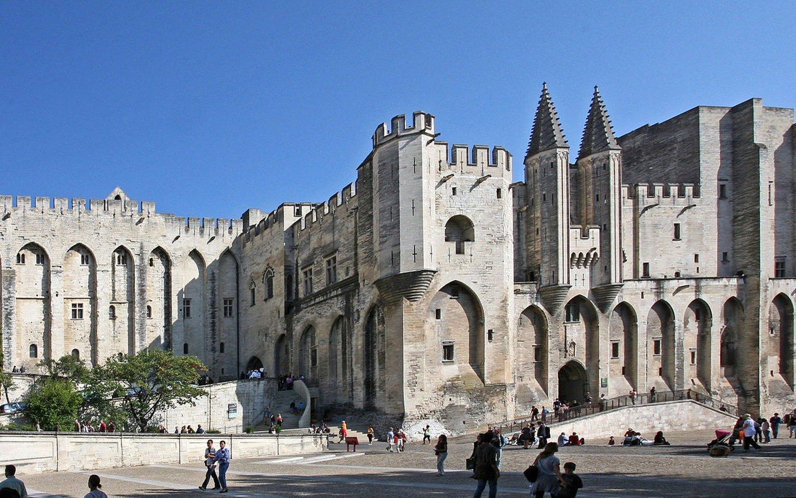 Fortified stone facade of the Palais des Papes with crenellated towers and visitors below