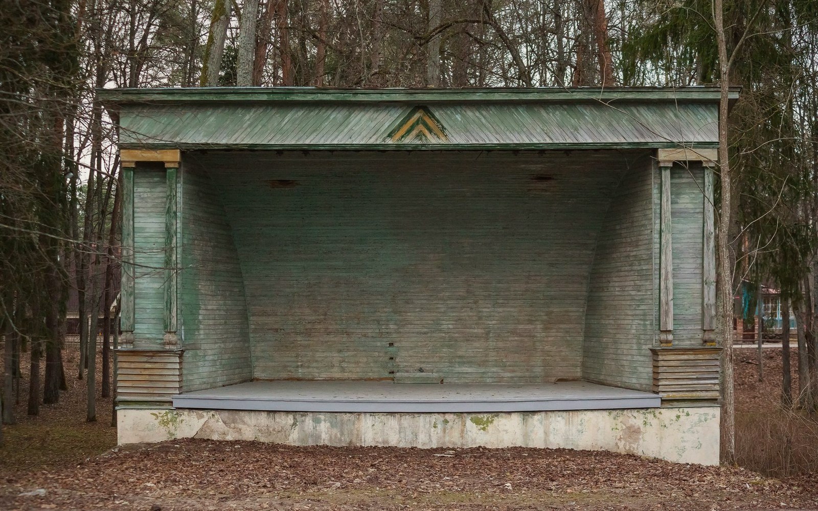 Weathered green wooden bandstand with columned canopy stands empty in a forest clearing